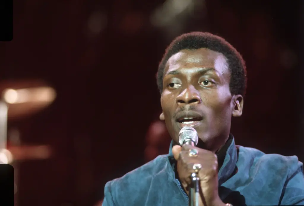 Jimmy Cliff durante show em 1974. Ele está segurando um microfone e cantando