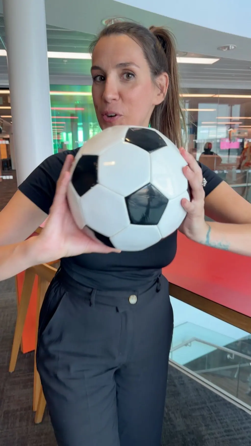 Alicia Hernández, con el pelo largo recogido en una coleta, vestida de negro y soteniendo una pelota de fútbol con las dos manos