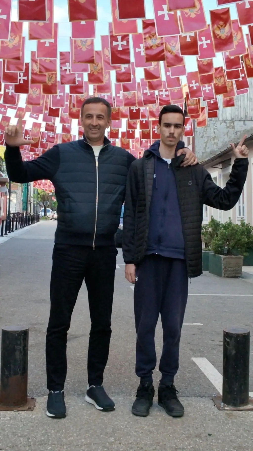 Dva muškarca stoje ispred zastava Crne Gore i prstima pokazuju slovo L.