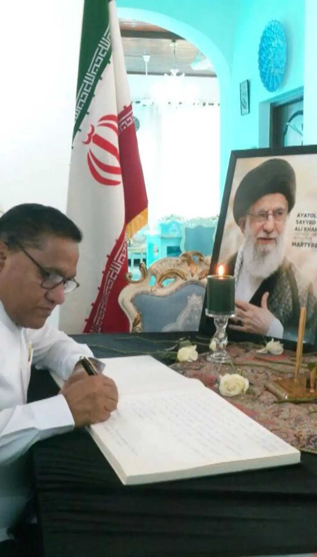 ඉරානයේ උත්තරීතර නායක අයතුල්ලා අලි කමේනිගේ ෆොටෝ එකක් ඉදිරිපිට සිට විදේශ අමාත්‍ය විදේශ අමාත්‍ය විජිත හේරත් ශෝක පොතේ අත්සන් කරයි.