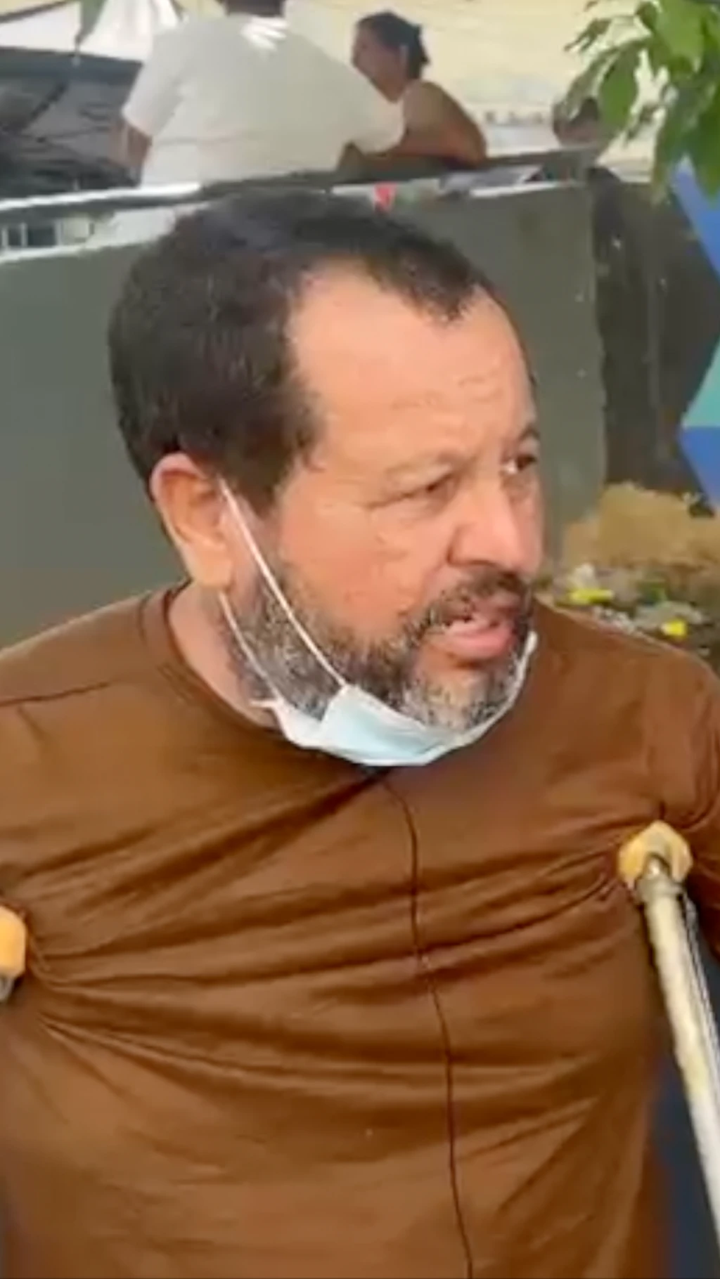 Un hombre con muletas, tiene barba y camisa marrón