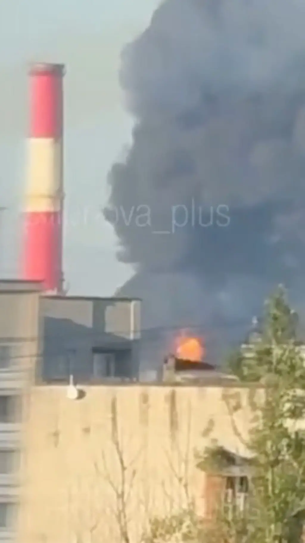Скриншот с видео очевидца удара по НПЗ: крыши домов, за ними - столб дыма и пламя огня.