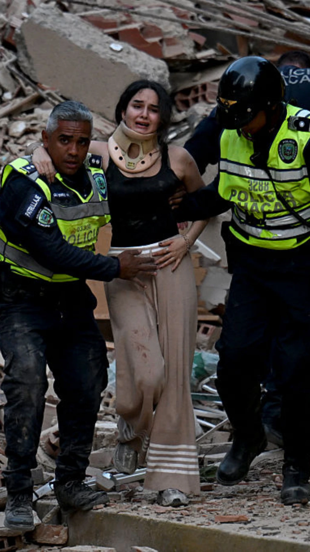 Una mujer con cuello ortopédico está siendo retirada por dos rescatistas de los escombros de un edificio colapsado