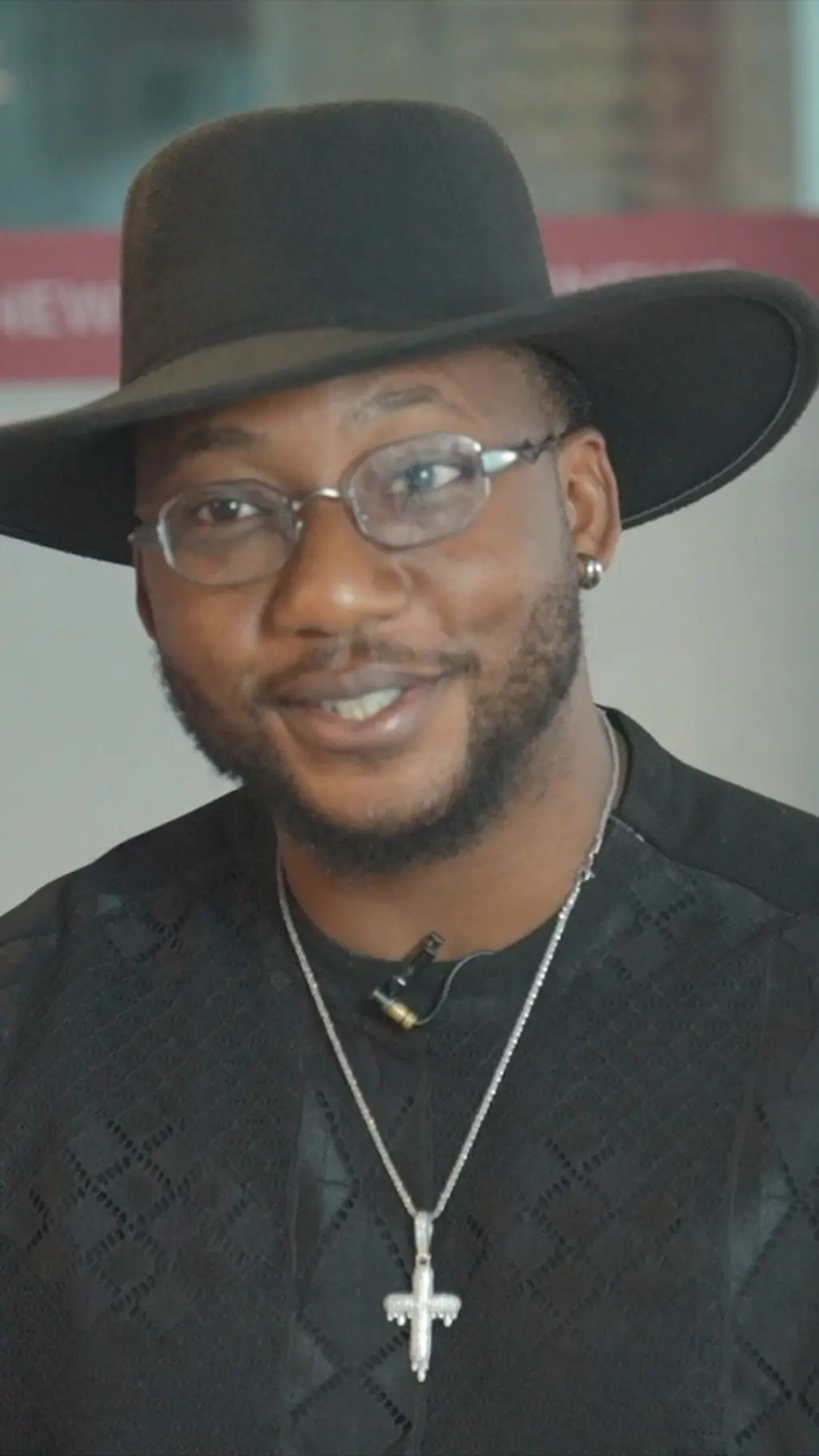 Abayomi Alvin wọ asọ shaati dudu, o de fila bẹnti gọ, o si fi ẹgba ọrun sọrun ati igo soju