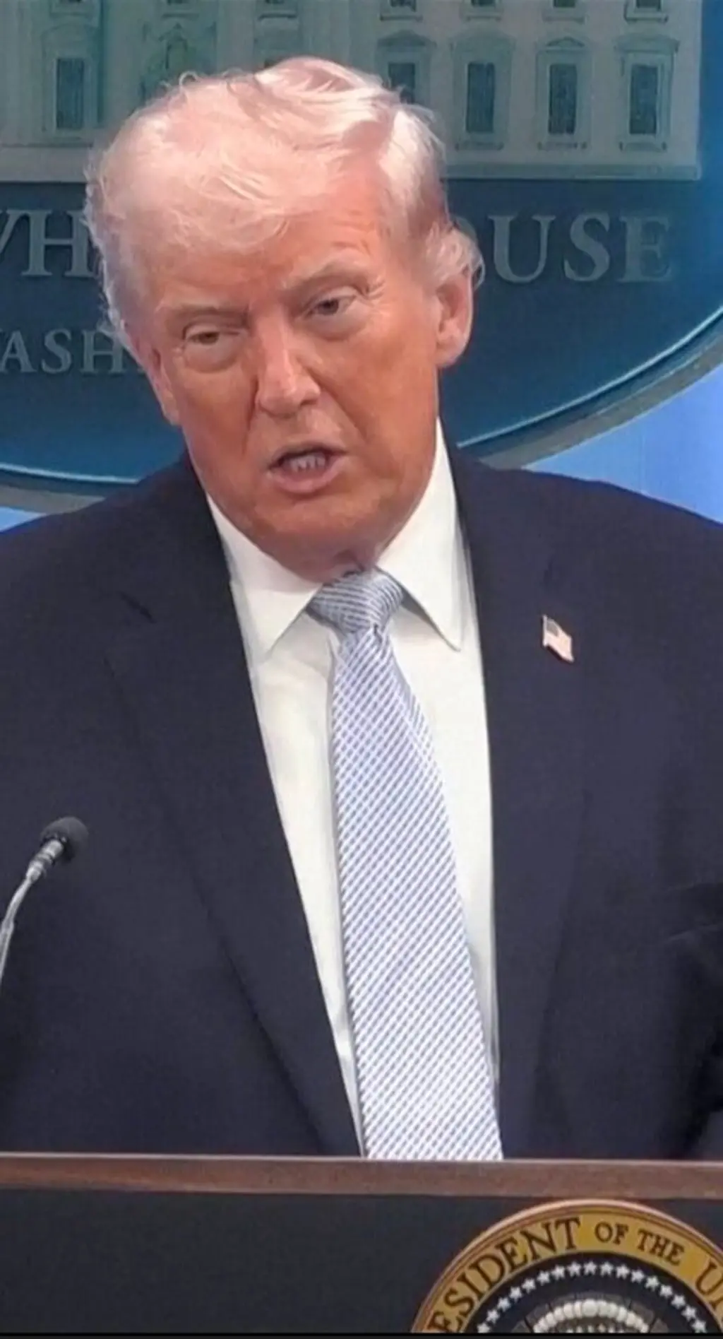 ලා නිල් පාටින් කොටු වැටුණු සුදු පැහැති ටයි එකක් පැළඳ, සුදු පැහැති කමිසයක් ඇඳ කළු කෝට් එකකින් සැරසී සිටින ඩොනල්ඩ් ට්‍රම්ප් මෙහි සිටී.