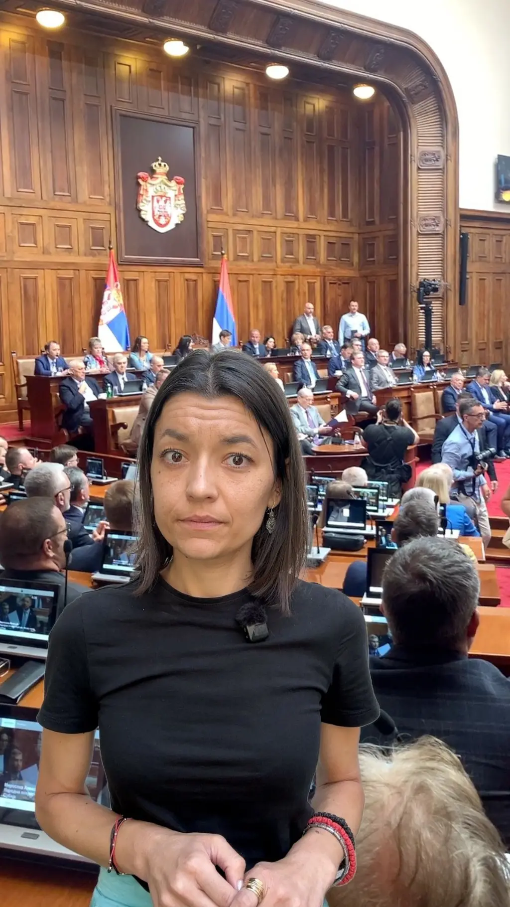 Novinarka gleda u kameru, iza nje sednica skupštine.