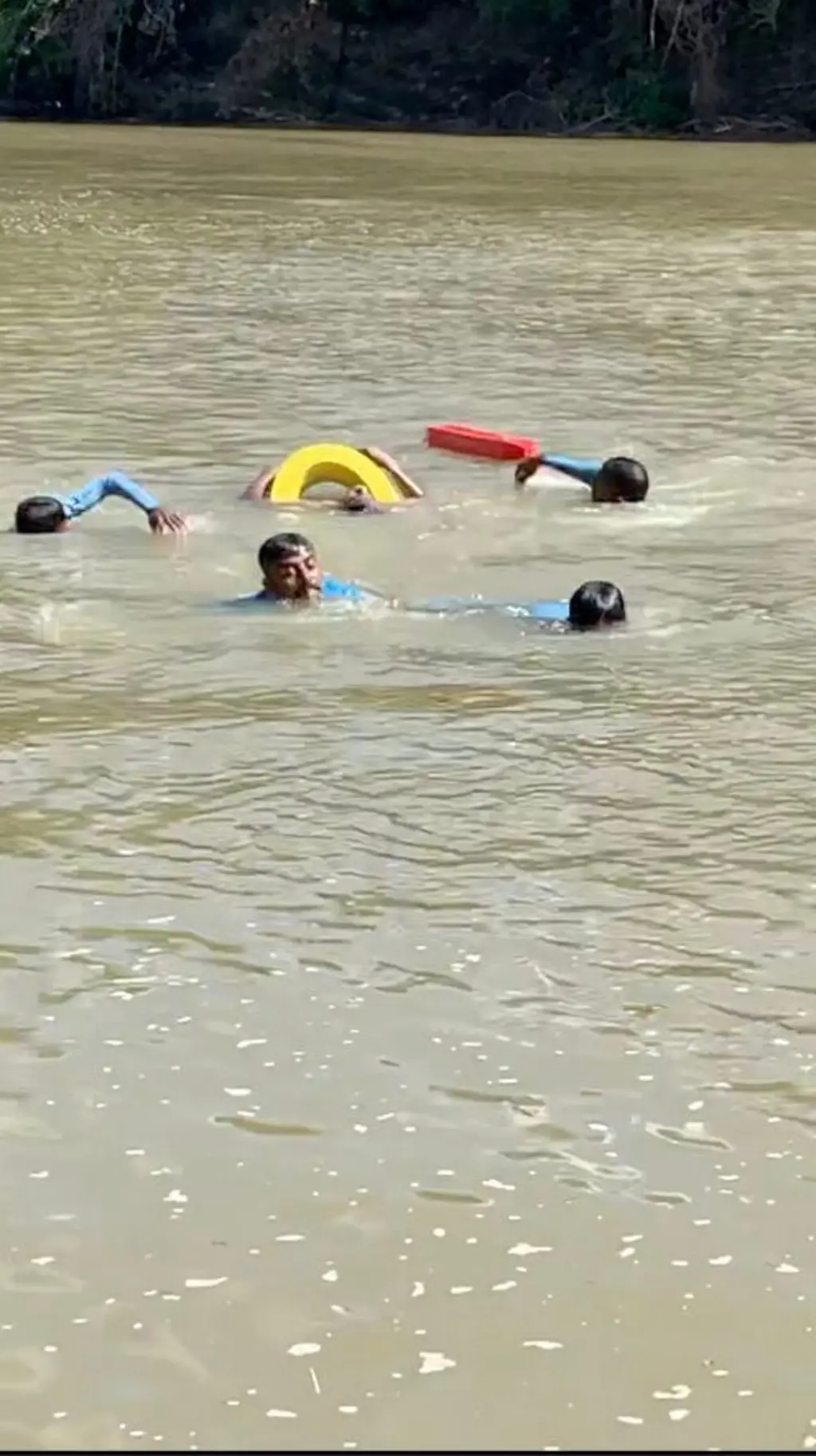 ගඟක පුද්ගලයින් හතර දෙනෙකු පිහිනන අතර කහ සහ රතු පති ටයර් දෙකක් පෙනේ.