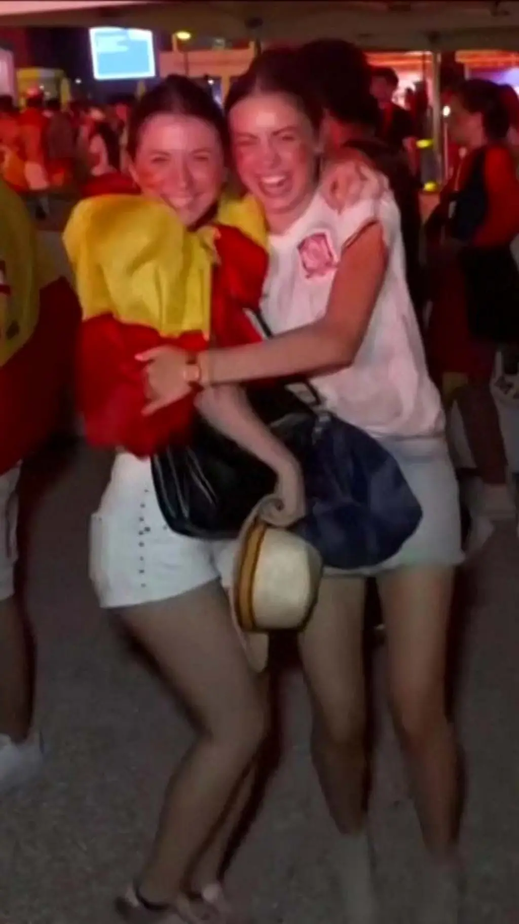 Dos mujeres ríen abrazadas, una lleva encima la bandera de España