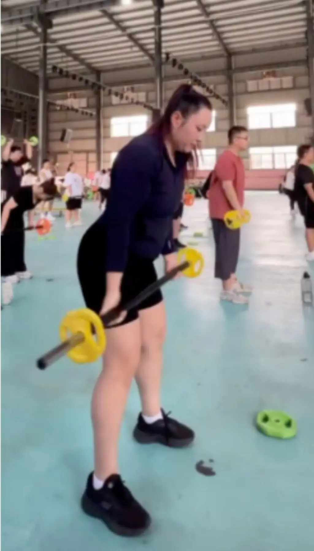 ව්‍යායාම මධ්‍යස්ථානයක කාන්තාවක් බර උසුලන ආකාරය පෙනේ.