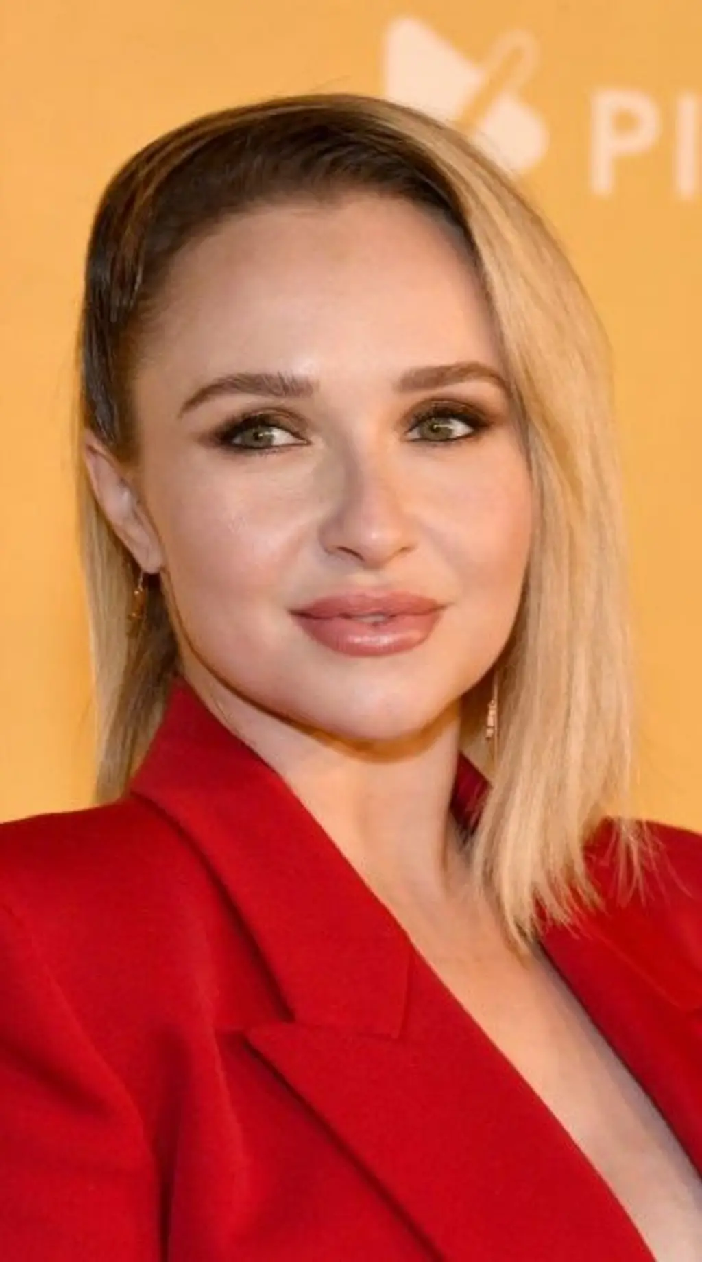 Hayden Panettiere é uma mulher loira, de olhos claros. Ela usa um casaco vermelho.