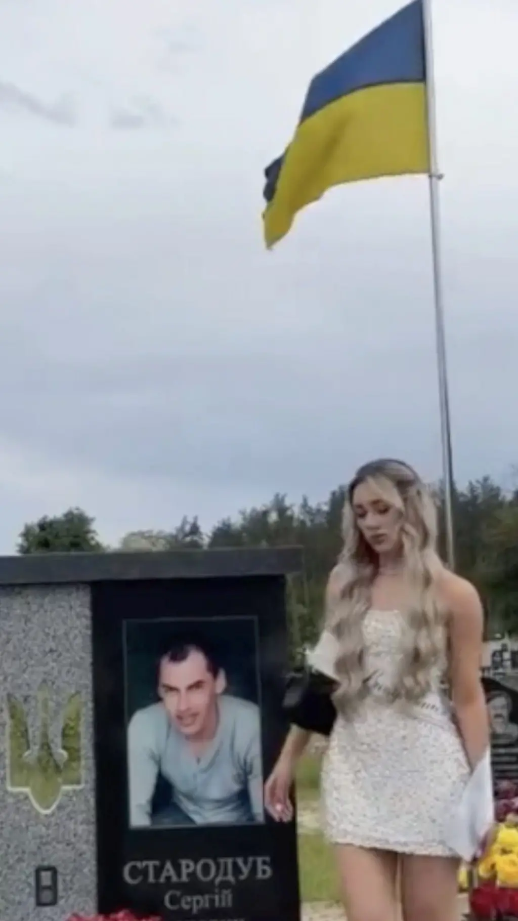 Ukraina bayrog'i ostidagi qarb, unda Starodub Serhiy deb yozilgan, va erkak kishining rasmi bitilgan. Bitiruvchi qiz qarb yonida yerga qarab turibdi.