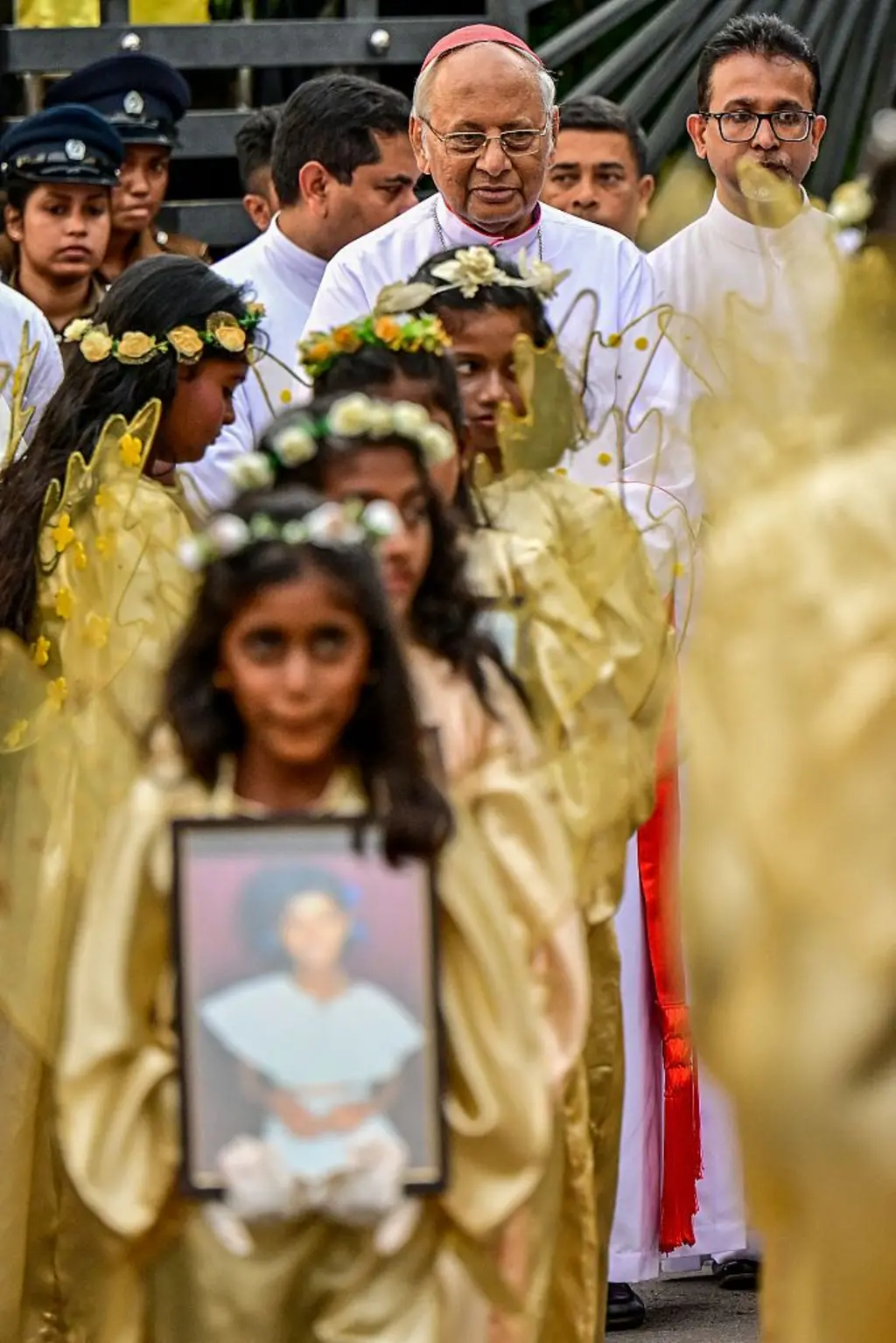 දැරියන් පිරිසක් පාස්කු ප්‍රහාරයෙන් මිය ගිය අයගේ ෆොටෝ රැගෙන පෙළට ගමන් කරන අතර කාදිනල් හිමියන් ඇතුළු පිරිසක් පසුපසින් සිටී.