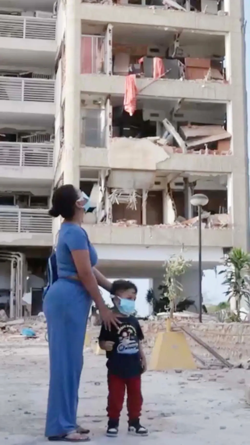 Una mujer y un niño, ambos con tapabocas, frente a un edificio residencial dañado por los terremotos en Venezuela