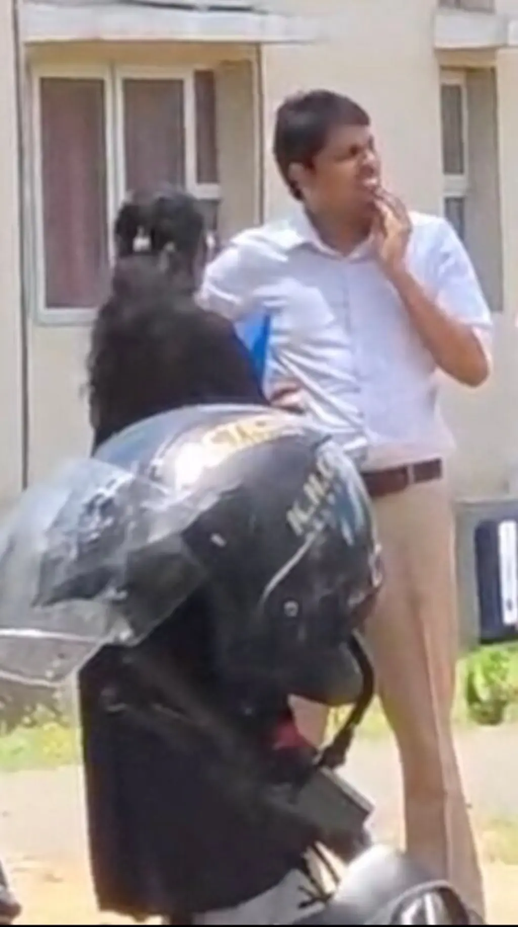 කාන්තාවක් අසල හිටගෙන සිටින පුද්ගලයෙකු කම්මුලට අත තියාගෙන ඉවත බලාගෙන සිටී.