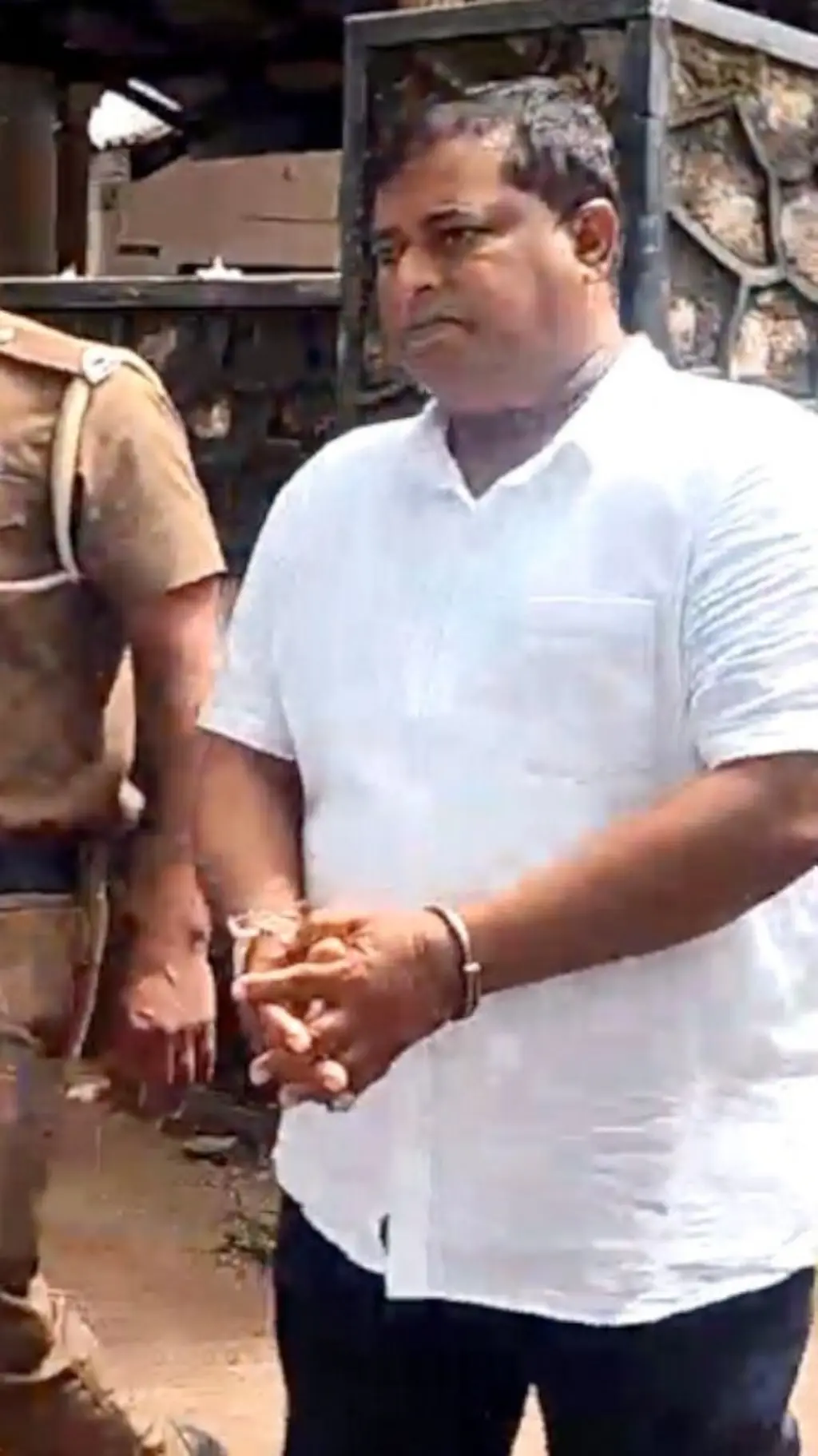 සුදු කමිසයක් ඇඳ සිටින පුද්ගලයෙකුගේ අතට මාංචු දමා තිබේ.