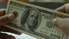 Uma pessoa segura uma nota de cem dólares dos EUA