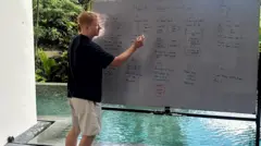 Sol, vestindo uma camiseta preta e shorts bege, escreve em um quadro branco em frente a uma piscina.