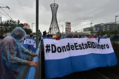 Grupo de pessoas com cartaz “Onde está o dinheiro?”, nas cores da bandeira hondurenha.