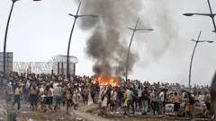 Centenas de pessoas que cruzaram a fronteira se reúnem em volta de uma estrutura incendiada no enclave espanhol de Ceuta, no norte da África