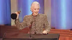 Jessica Tandy, de roupa com motivo floral, recebe o Oscar de melhor atriz de 1990