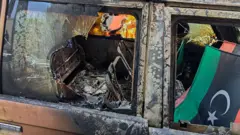 علم ليبيا معلق داخل سيارة محترقة