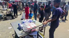 Palestinos observam pacotes de farinha à venda em um mercado improvisado na área de Mawasi, em Rafah, em meio à disparada nos preços dos alimentos já escassos