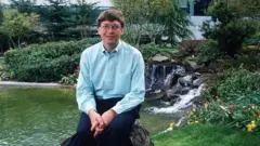 Bill Gates jovem, sentado sobre uma pedra em frente a uma pequena cascata e lago