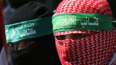 Abu Obayda wearing a red keffiyeh around his head that keeps his identity secret 