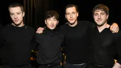 Joseph Quinn, Barry Keoghan, Harris Dickinson e Paul Mescal com os braços em volta dos ombros uns dos outros, todos vestidos de preto, na CinemaCon
