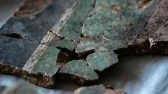Una imagen de cerca de al menos 10 fragmentos de yeso que han sido unidos. En el lado derecho de la imagen se encuentra la sección rosa, luego una delgada línea divisoria negra y una banda verde pálido más gruesa. Hacia la izquierda de la imagen hay una fina línea divisoria blanca y luego una gruesa banda negra.