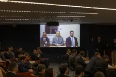 Braga Netto aparece em telão ao lado de dois advogados; o telão está em uma sala de audiência do STF com dezenas de pessoas sentadas