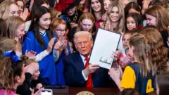 署名した大統領令を掲げるドナルド・トランプ米大統領の周りに、スポーツのユニホームを着た少女たちが集まっている
