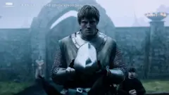 Bir diziden posterde, bir orta çağ şövalyesi elinde miğfer tutuyor ve sert şekilde kameraya bakıyor. Arkada bir kale var.