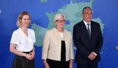 İki kadın ve bir erkek bir haritanın önünde poz veriyor.