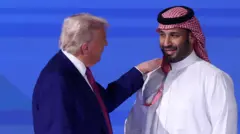 ترامب يرتدي بدلة كحلية رسمية وقميصاً أبيض وربطة عنق حمراء، يضع يده على كتف بن سلمان وهو يرتدي اللباس التقليدي السعودي الأبيض وشماغاً أحمر ويبتسم. خلفهما خلفية بيضاء.