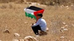 A boy holds a Palestinian flag during a demonstration against what Palestinians say is Israel's confiscation of their land, as Isareli security forces stand guard, in Raba, near Jenin, in the Israeli-occupied West Bank July 18, 2025.