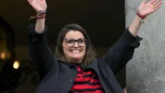 María José Pinto cumprimentando seus seguidores em uma janela