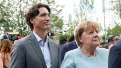 Justin Trudeau e Angela Merkel na inauguração. Ele veste terno cinza com camisa clara e ela um casaco azul-claro