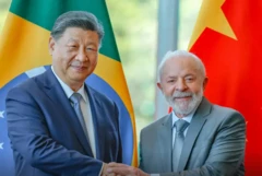 Xi Jinping à esquerda e Lula à direita apertando as mãos com as bandeiras dos dois países ao fundo