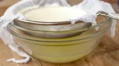 Imagem mostra tigela com soro do leite e uma peneira em cima com queijo