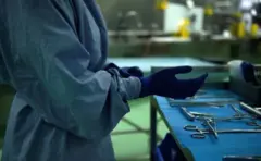 Uma médica colocando uma luva. Há vários instrumentos cirúrgicos ao lado