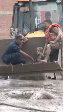 Женщина едет в ковше бульдозера со спасателями 