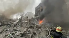 Зруйновані будинки, пожежа, видно рятувальника