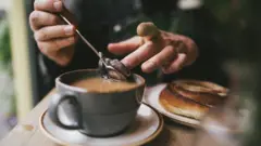 A tea drinker removes the tea bag from their cup