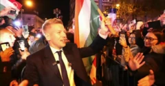 Peter Magyar onde sonriente una bandera de Hungría rodeado de seguidores en la celebración de su triunfo electoral en Budapest. 