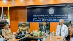 මහජන ආරක්ෂක අමාත්‍ය ආනන්ද විජේපාල, අමාත්‍යංශ ලේකම්වරයා, පොලිස්පතිවරයා ඇතුළු තවත් නිලධාරීන් සිටින ඡායාරූපයක්