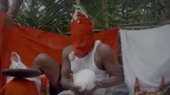 A man who claimed to sell human organs, his face covered with a festive red cloth, holding an object in his hands wrapped in a white cloth