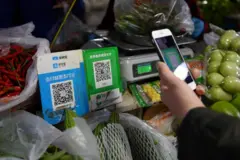 Una mano sostiene un celular mientras escanea un código QR en una venta de vegetales y verduras en un mercado en China.