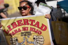 Uma mulher usando óculos escuros segurando um cartaz: 'Liberdade para meu filho preso em 03 de dezembro de 2022'.