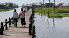 Hai cô gái nhìn từ phía sau đi trên cầu đi bộ ở làng Mang Thawk, hồ Inle, Miến Điện